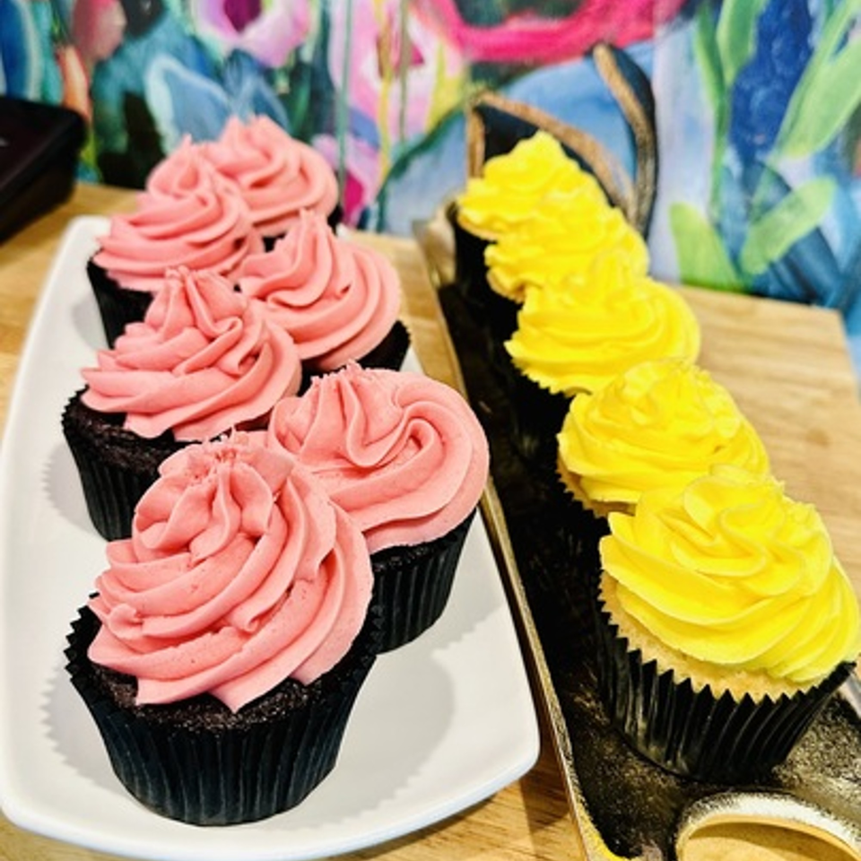 Pink and yellow frosted cupcakes on white and black trays, with a colorful background.