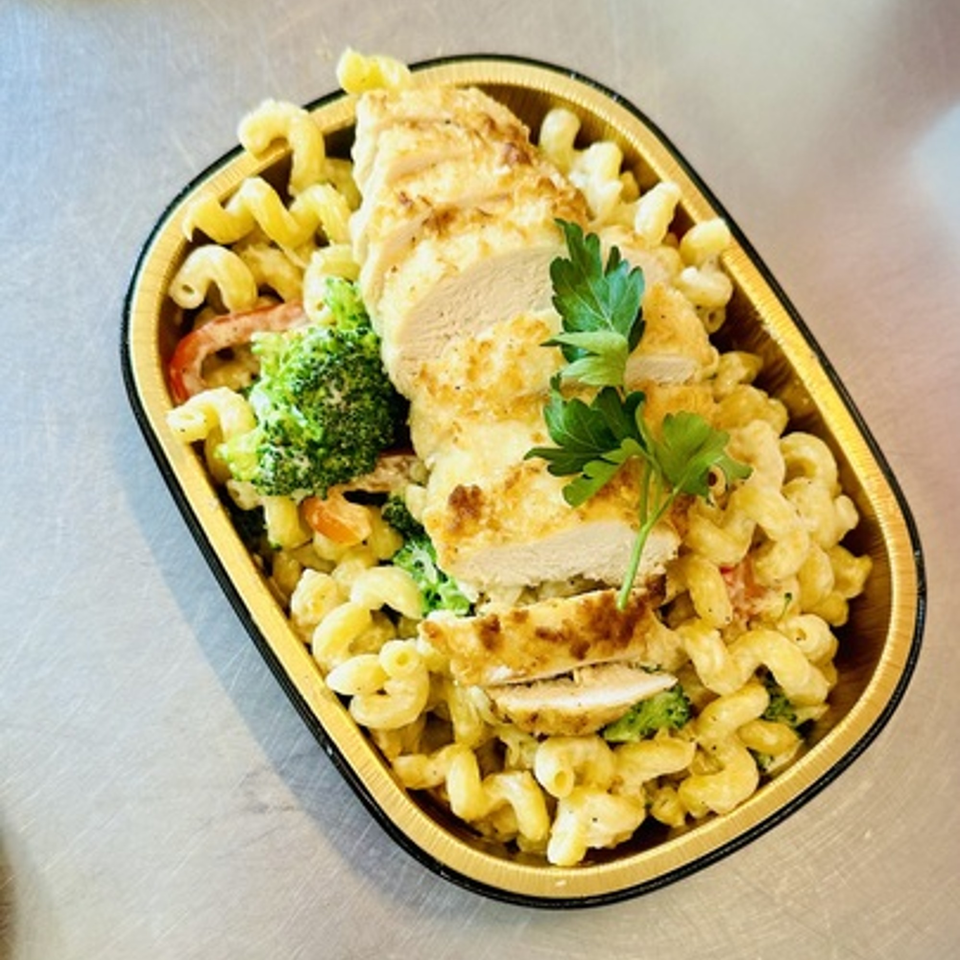 Creamy pasta with sliced chicken breast, broccoli, and red peppers in a gold foil container.