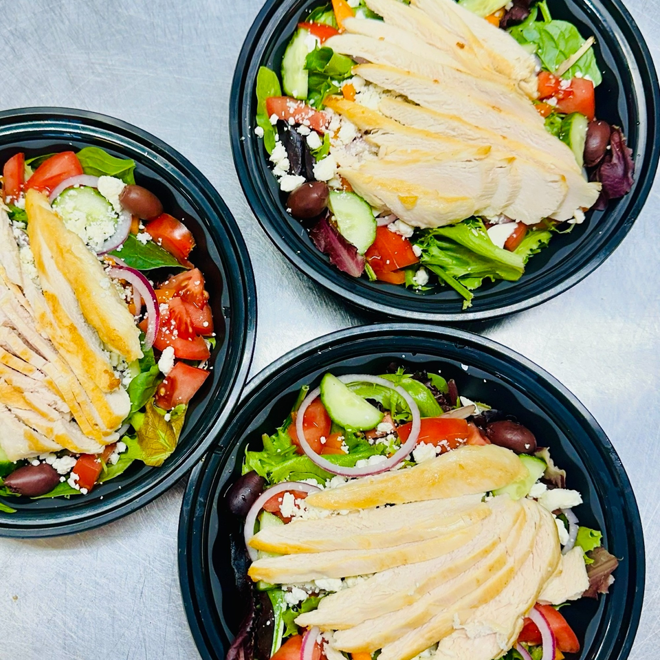 Three Hello Good Pie salads with sliced chicken, mixed greens, tomatoes, cucumbers, olives, and feta.