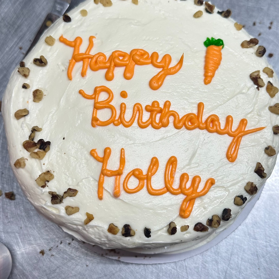 A Hello Good Pie carrot cake with white frosting, walnuts, and "Happy Birthday Holly" in orange icing.