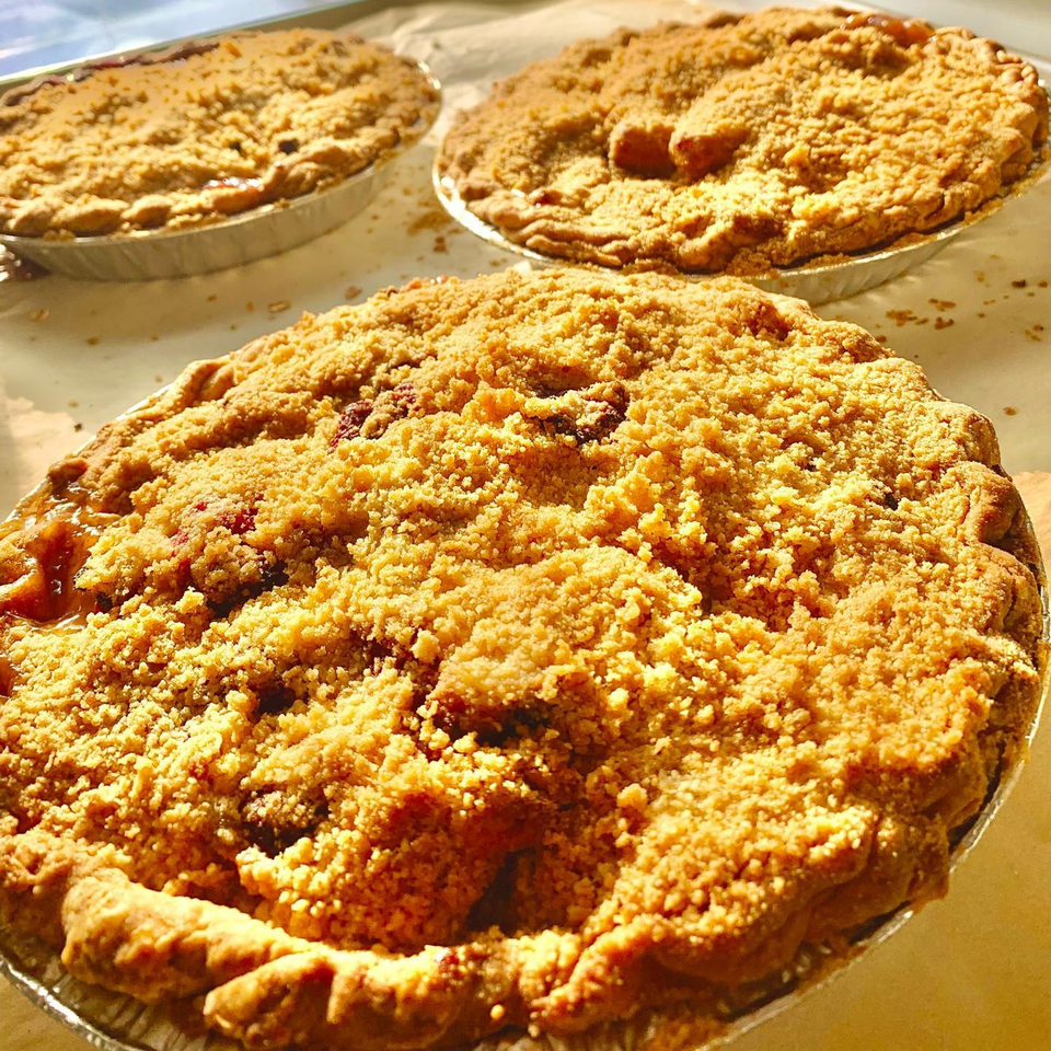 Three Hello Good Pie crumble-top fruit pies in foil tins, glistening in warm sunlight.