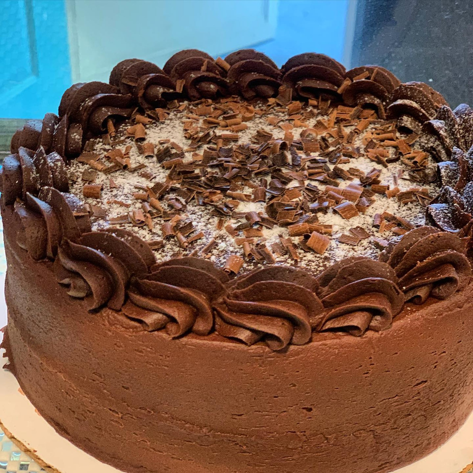 A Hello Good Pie chocolate cake with chocolate frosting, shavings, and powdered sugar.